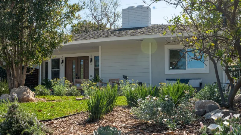 Charming house surrounded by lush green garden with flowers and shrubs in bright daylight.