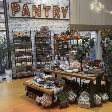 Cozy pantry display with shelves of preserves, jams, and autumn-themed decor in a rustic store setting.