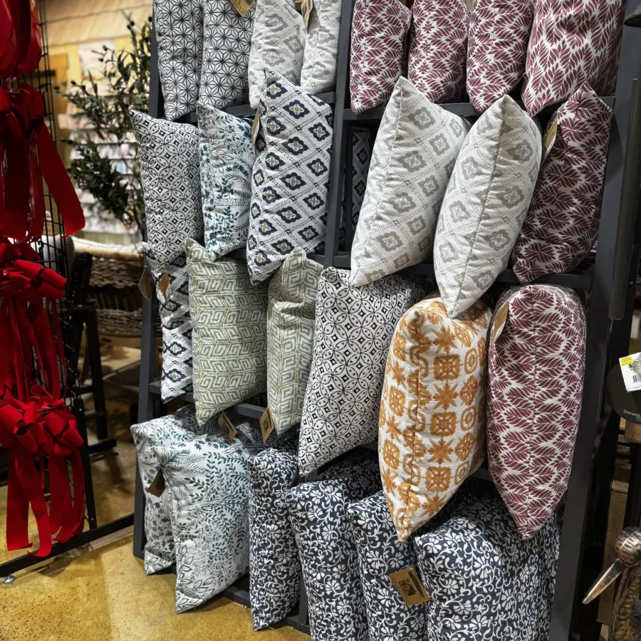 Display of decorative pillows with various intricate patterns and colors on a black metal rack.