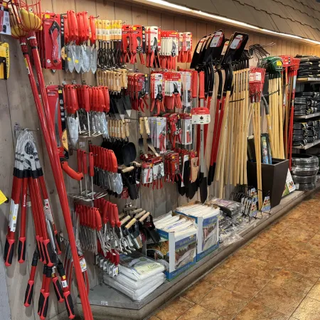 Store aisle displaying various gardening tools including pruners, shovels, rakes, and gloves neatly arranged on shelves.