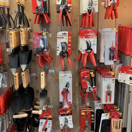 Wall display of various gardening tools including pruners, shears, trowels, and cultivators with wooden handles.