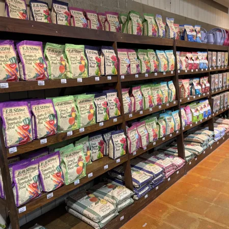 Shelves stocked with bags of E.B. Stone organic tomato, vegetable, and fruit food in a garden supply store
