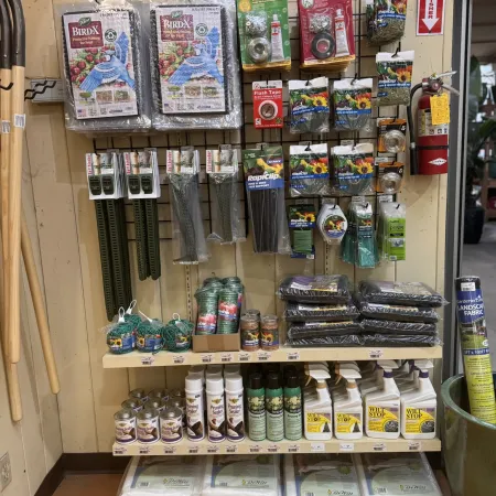 Gardening supplies on shelves including protective netting, plant anchor kits, pruning sealers, and landscape fabric.