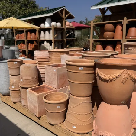Outdoor display of various terracotta and ceramic plant pots in different shapes and sizes under sunlight.