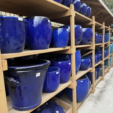 Shelves filled with various sizes of shiny blue ceramic pots and planters in an outdoor garden center.