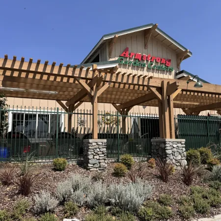 Exterior of Armstrong Garden Center with wooden pergola, stone pillars, and landscaped plants under clear blue sky