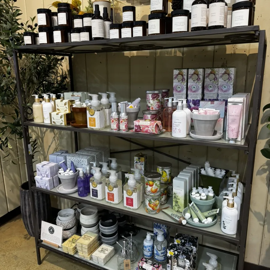 Metal shelving unit displaying various scented candles, lotions, soaps, and gift sets in a retail store.