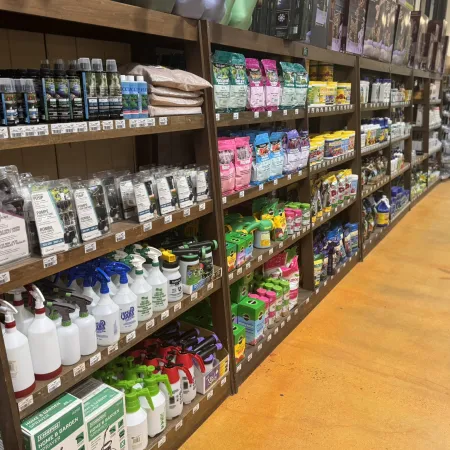 Wooden shelves stocked with gardening sprays, fertilizers, plant nutrients, and garden care products in a store aisle.