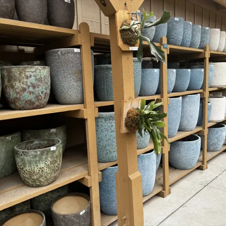 Rows of ceramic and stone textured plant pots in various colors displayed on wooden shelves in a garden store.