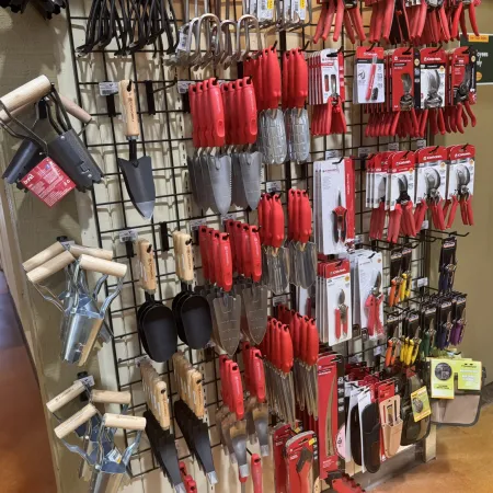 Display of various gardening tools including trowels, cultivators, pruning shears, and weeders with wooden and red handles.