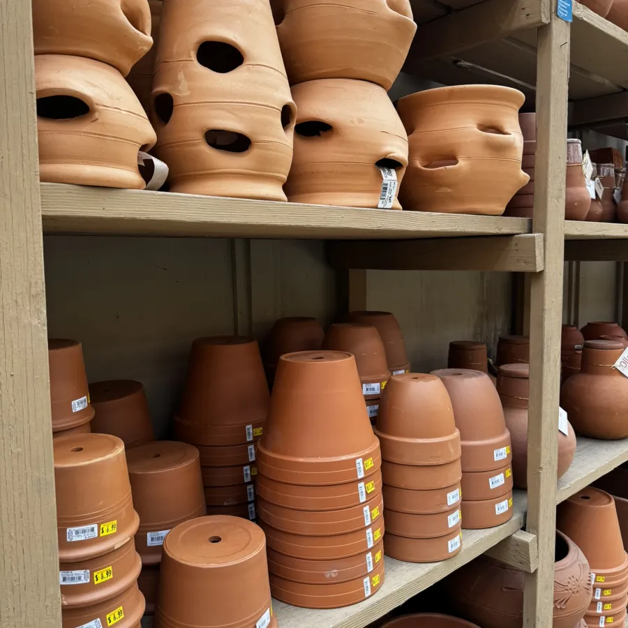 Shelves filled with various terracotta plant pots and clay gardening containers with price tags.