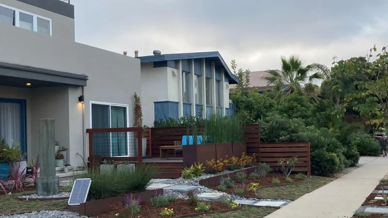 Modern residential street with drought-tolerant landscaping, concrete driveways, and a cloudy sky overhead.