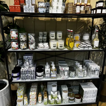 Display shelf stocked with candles, lotions, soaps, and decorative flowers in a cozy store setting.