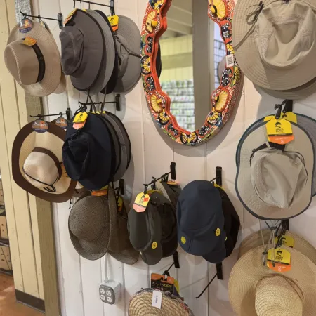 Variety of sun hats displayed on a white wooden wall with a colorful decorative mirror in the center.