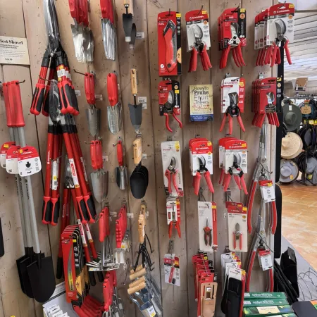 Display of various garden tools including pruners, shovels, trowels, and cultivators with red handles in a store.
