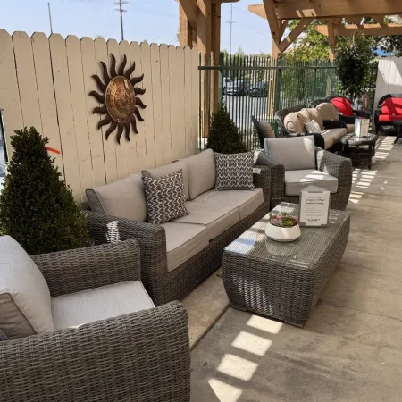Outdoor patio seating area with wicker furniture, gray cushions, decorative pillows, and a wooden sun wall hanging.