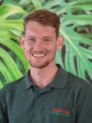 Smiling man wearing Armstrong Garden Centers green polo shirt with a leafy green background